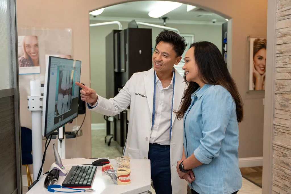 Dentist in white coat showing dental X-ray on a computer screen to a smiling woman in a dental office.
