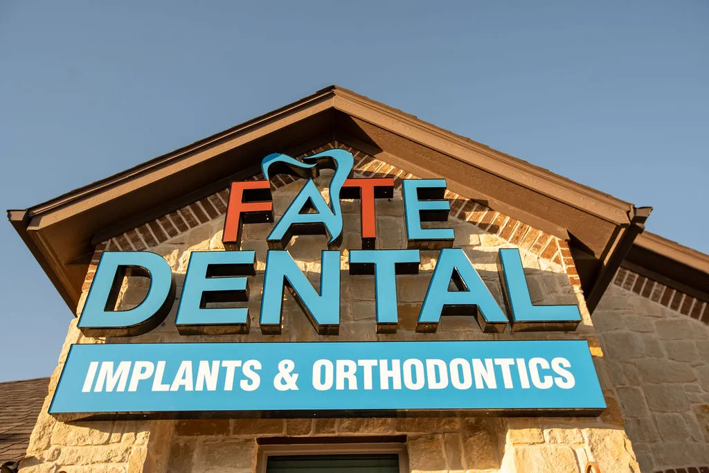 Sign on a building reading 'FATE DENTAL' with a tooth icon and 'IMPLANTS & ORTHODONTICS' underneath.