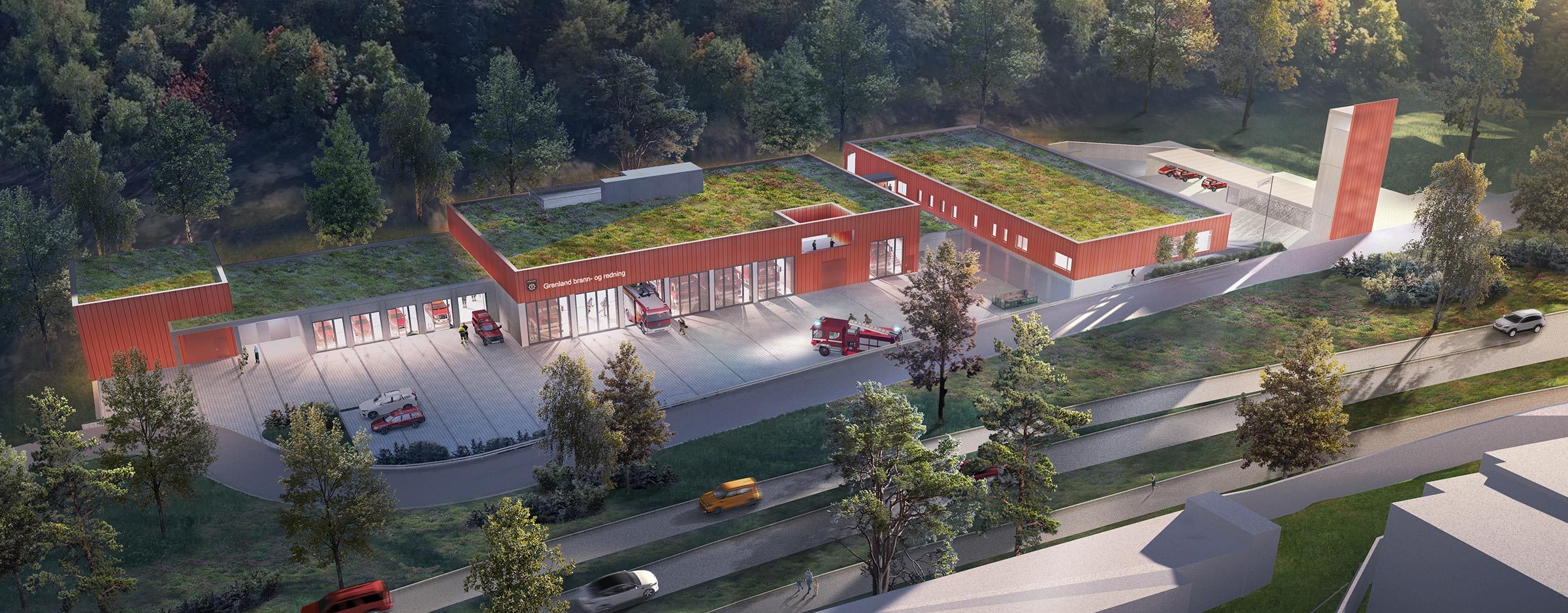 Aerial view of a modern fire station with red buildings and green roofs surrounded by trees, with fire trucks parked outside.
