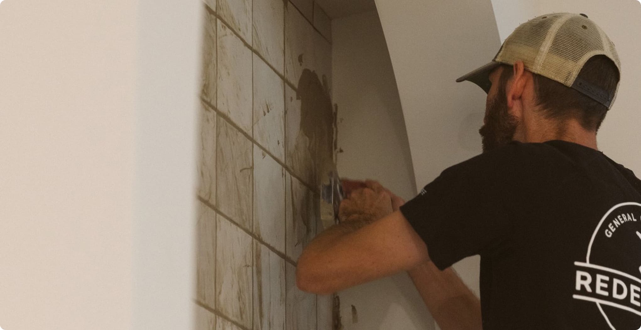 A man in a black shirt and a brown hat painting a brick wall.