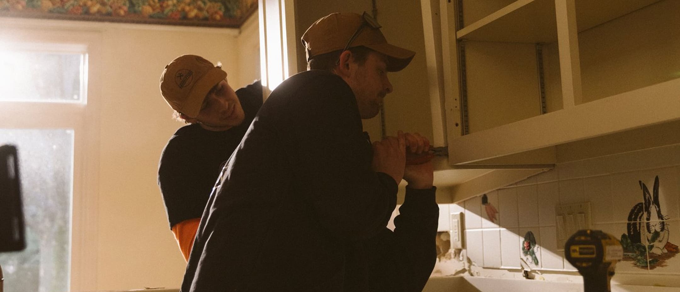 A couple of men standing next to each other in a kitchen.