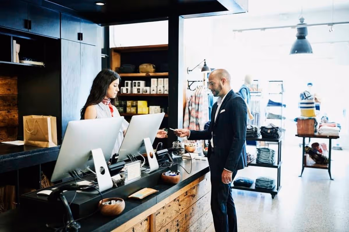 Customer in suit paying a cashier at a modern retail store with clothing and products display.