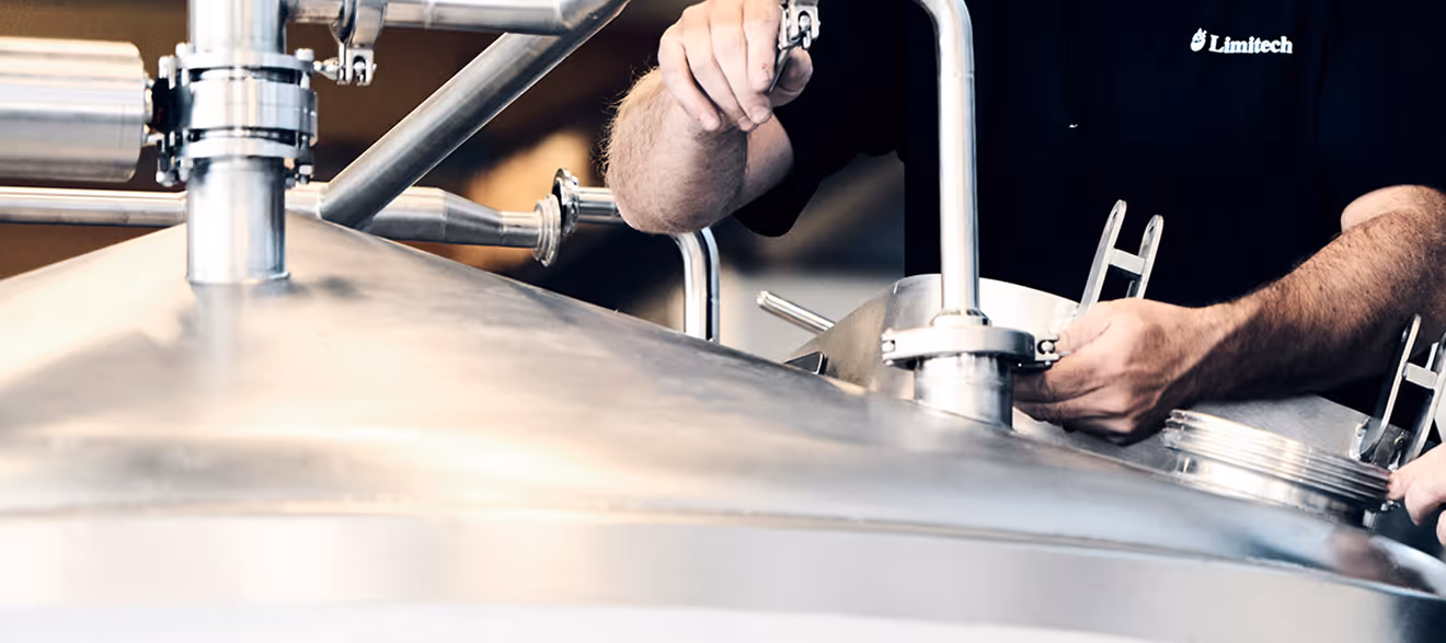 Person adjusting metal pipes and valves on large stainless steel industrial equipment.