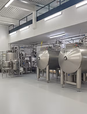 Large stainless steel industrial tanks and pipes in a clean, spacious factory setting.