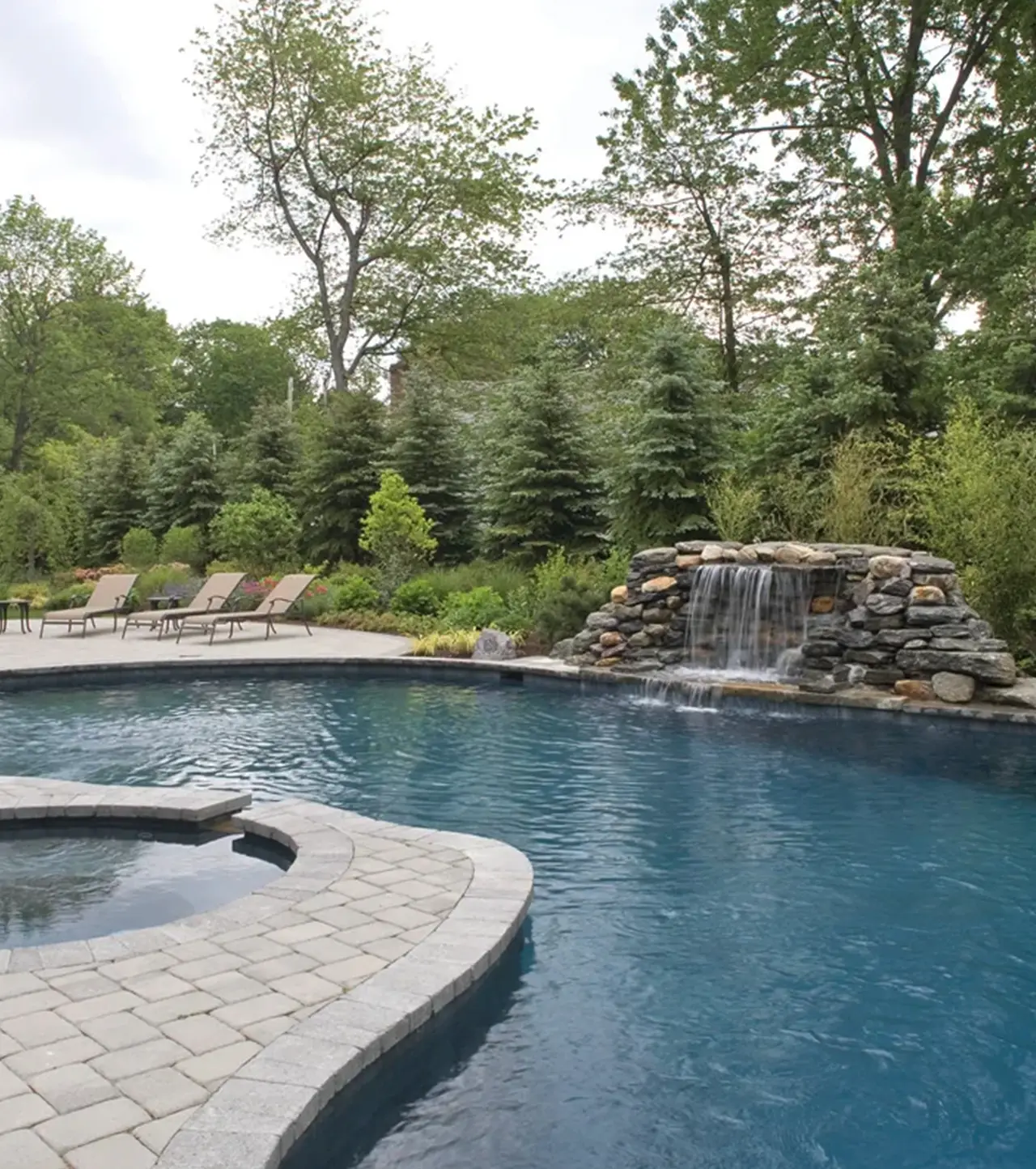 Backyard pool with a rock waterfall and spa at a private residence surrounded by mature trees