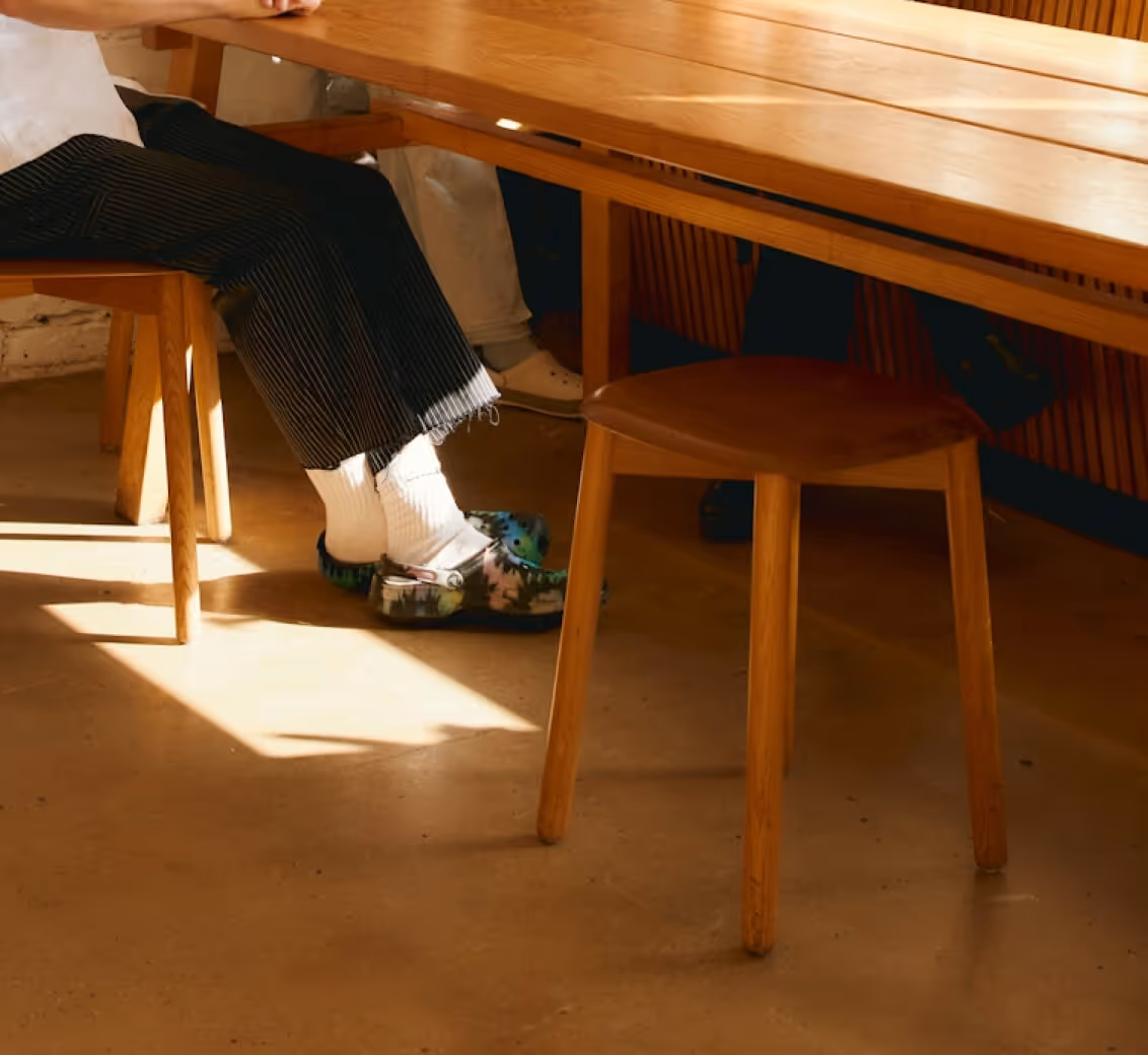 Person sitting at a wooden table wearing black striped pants, white socks, and colorful crocs shoes.