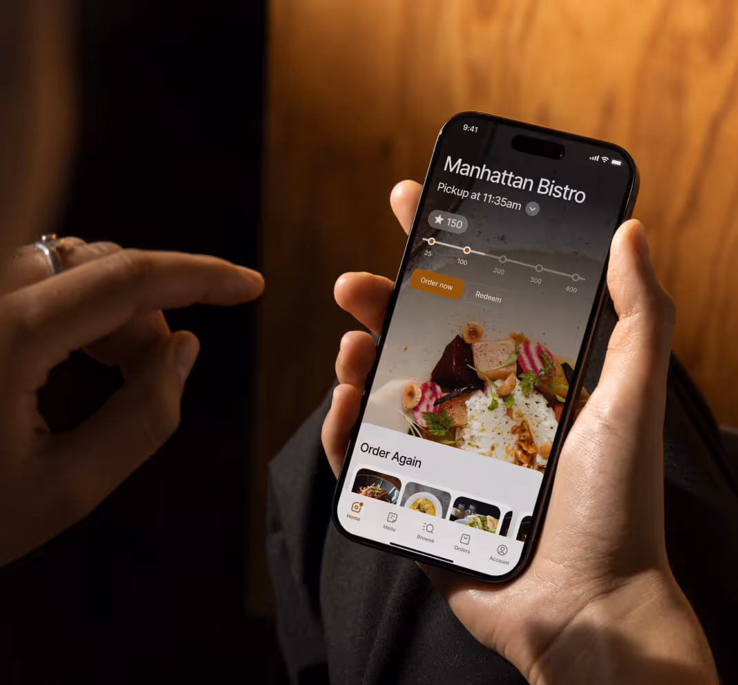 Hand holding a smartphone displaying a food ordering app for Manhattan Bistro with pickup time and order again options.
