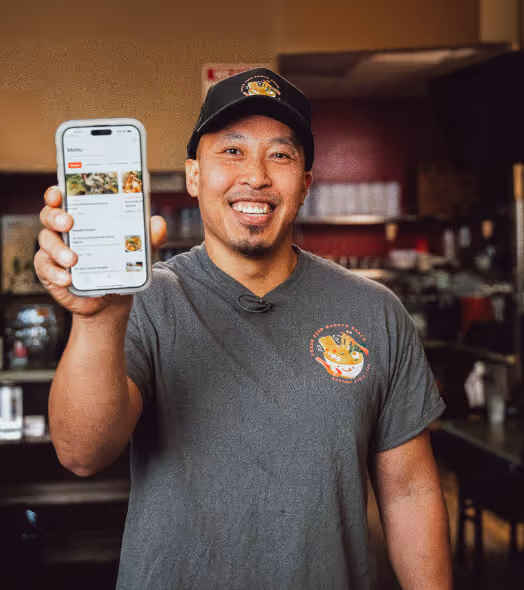 Smiling man wearing a hat and gray shirt holding a smartphone displaying a restaurant menu app.