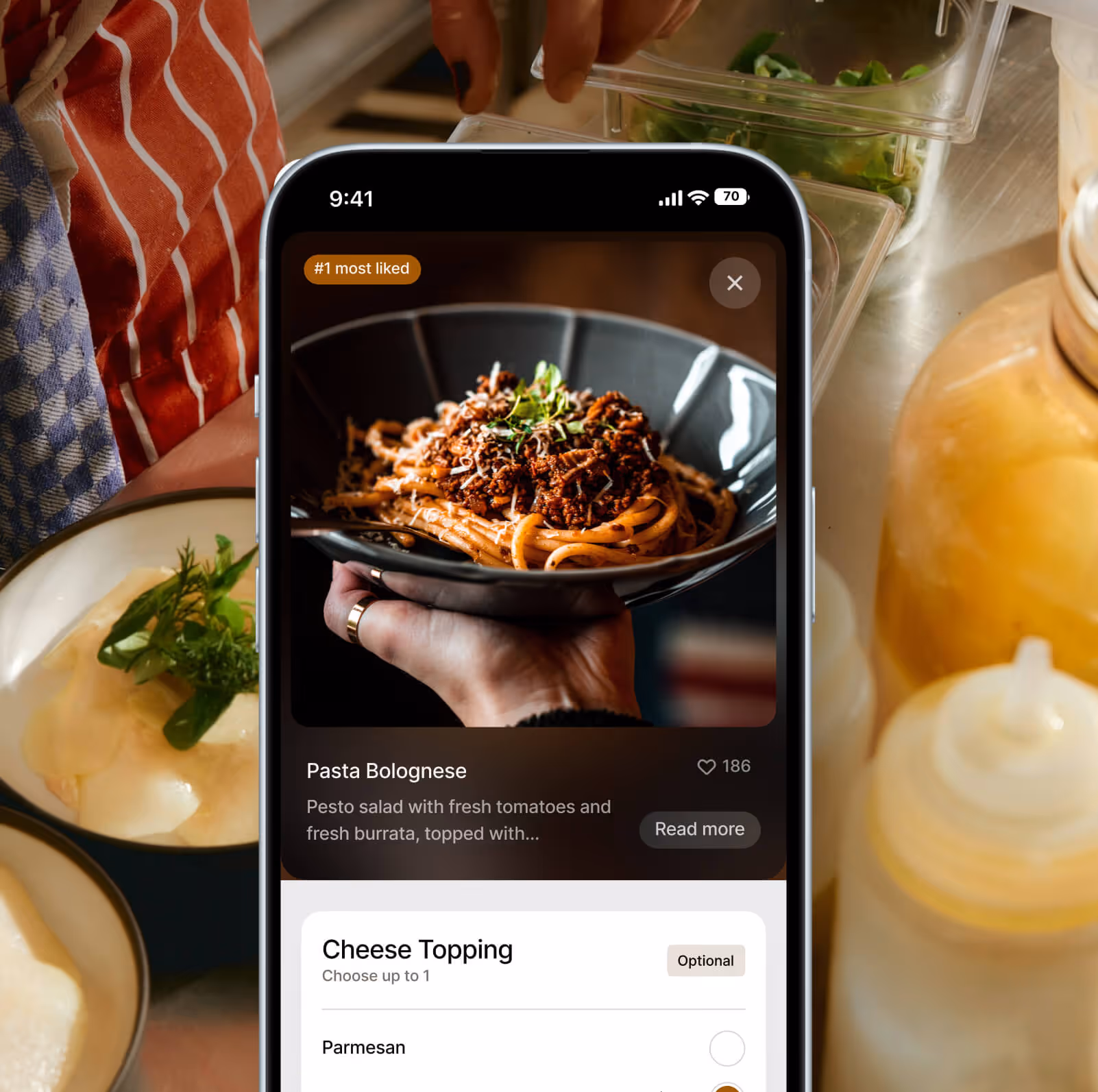 Smartphone displaying a food app with a Pasta Bolognese dish labeled as #1 most liked and an option to add Parmesan cheese topping.