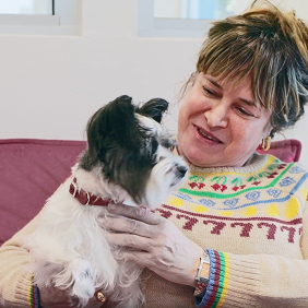 Woman smiling and holding a small black and white dog while sitting on a couch.