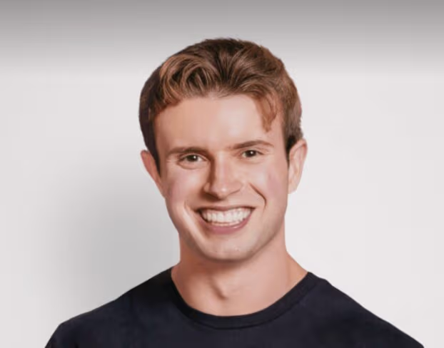 Smiling young man with short wavy brown hair wearing a black shirt against a plain background.