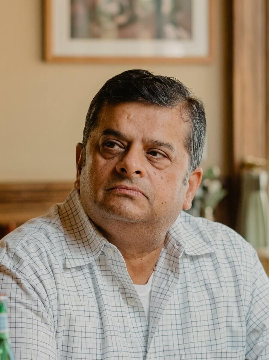 Middle-aged man with short dark hair wearing a white checkered shirt, looking to the side indoors.