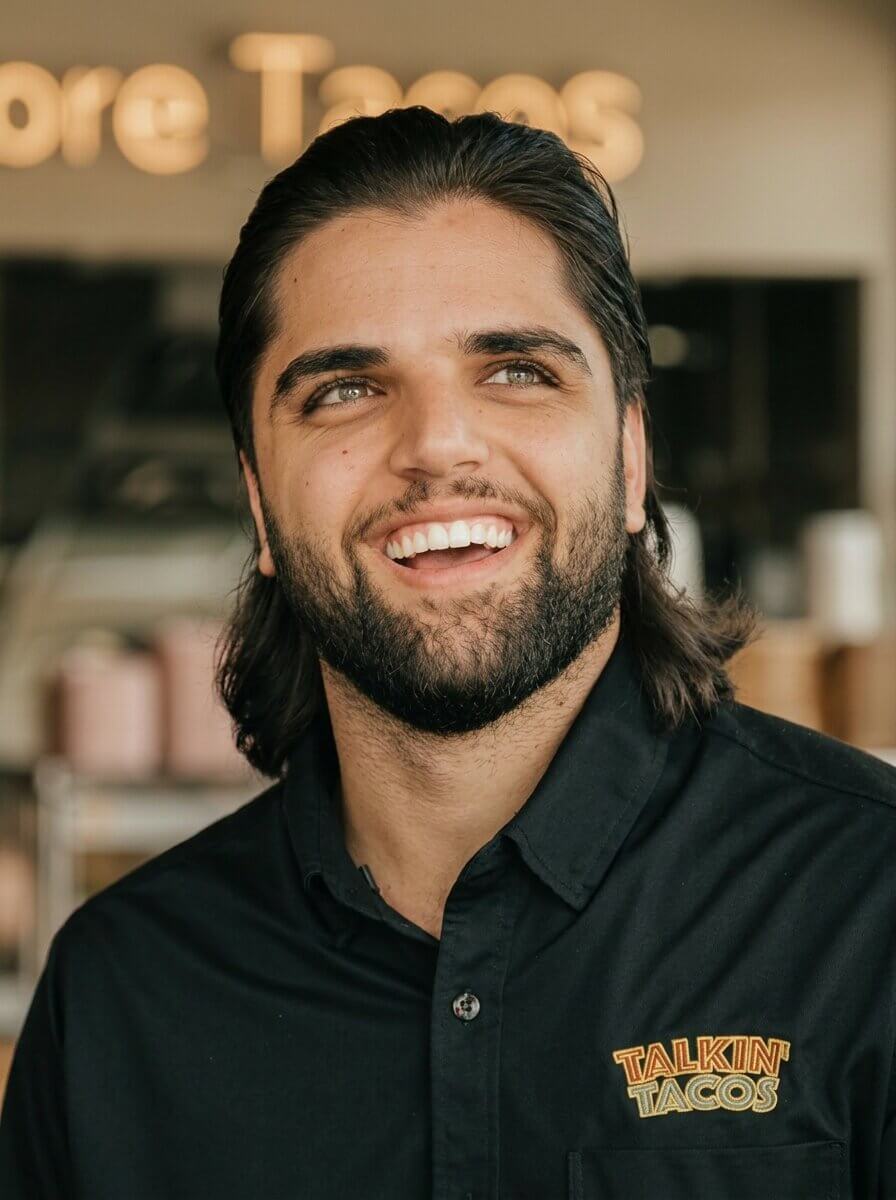 Smiling man with dark hair and beard wearing a black shirt with the Talkin' Tacos logo.