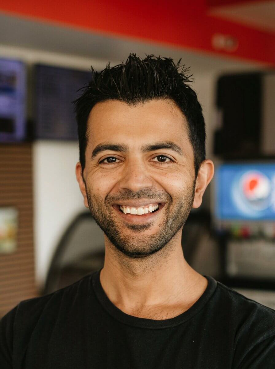 Smiling man with short black hair and beard wearing a black shirt in an indoor setting.