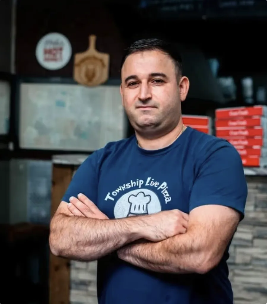 Sarkis Panossian of Township Line Pizza standing with arms crossed in front of stacked pizza boxes