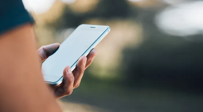 Hand hält ein modernes Smartphone mit leerem Bildschirm vor verschwommenem Hintergrund.