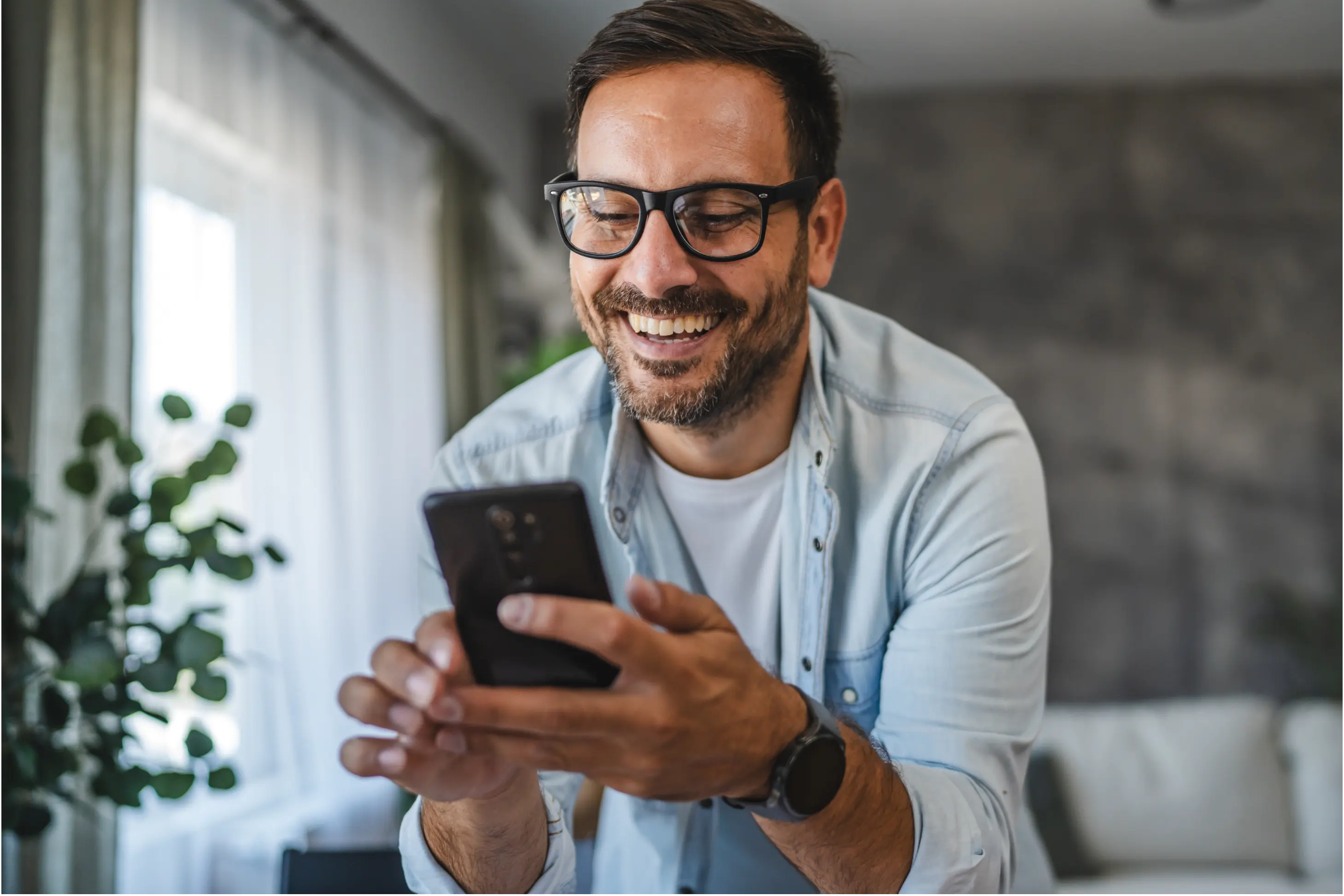 Lachender Mann hält Handy in der Hand.