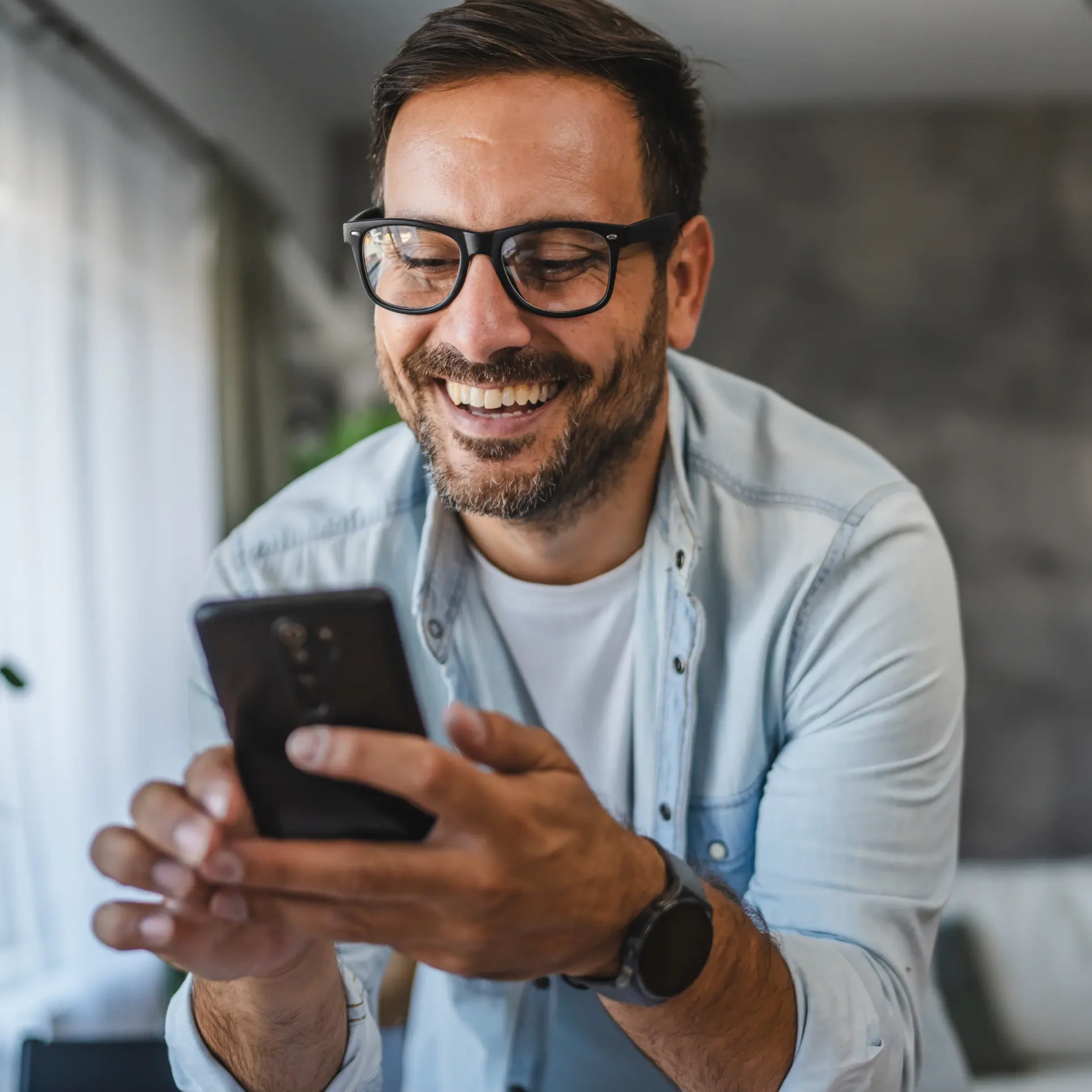 Lachender Mann hält Handy in der Hand.