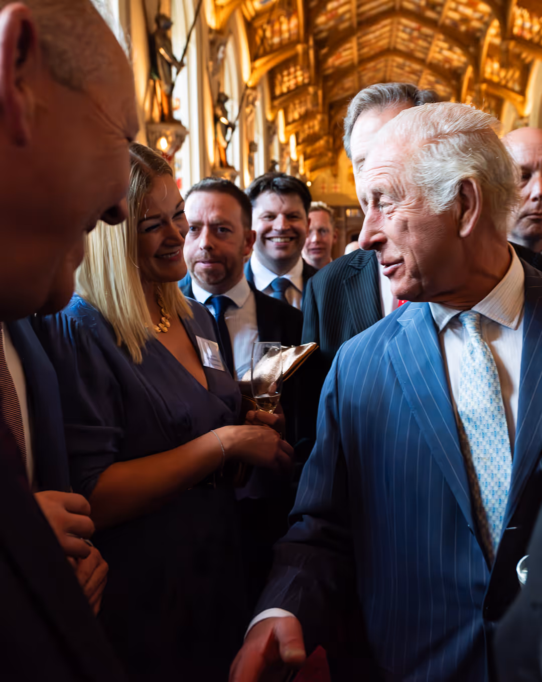 Group of professionally dressed people smiling and interacting in a grand room with arched ceilings.
