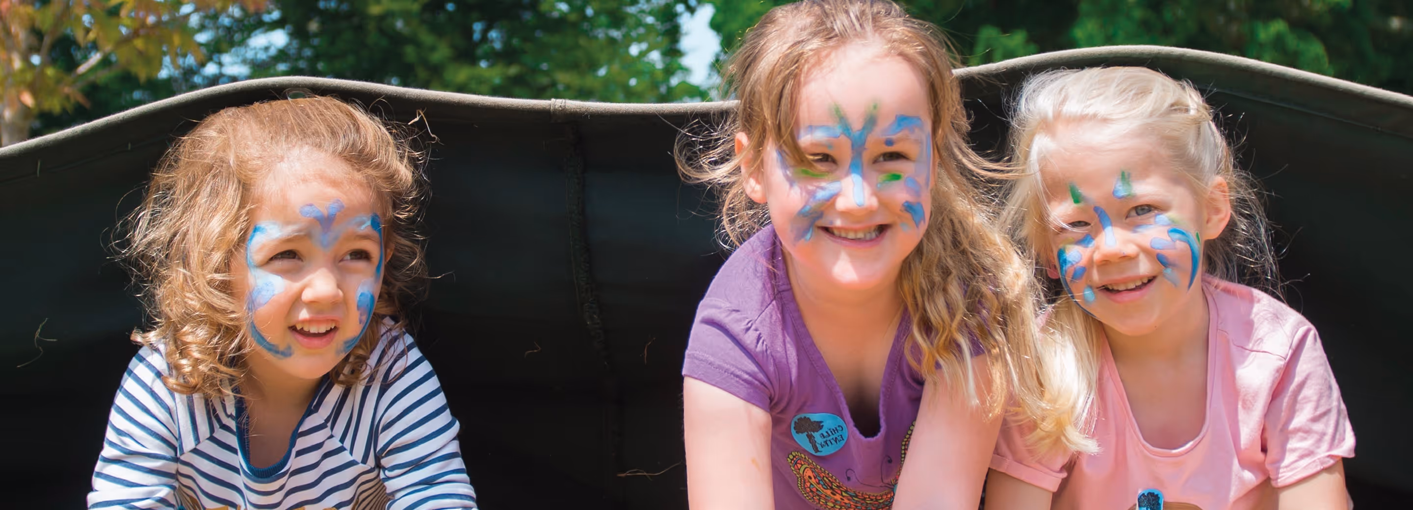 A man in a black jacket and blue jeans and a smiling woman in black sitting on rocks inside a greenhouse with plants around them.