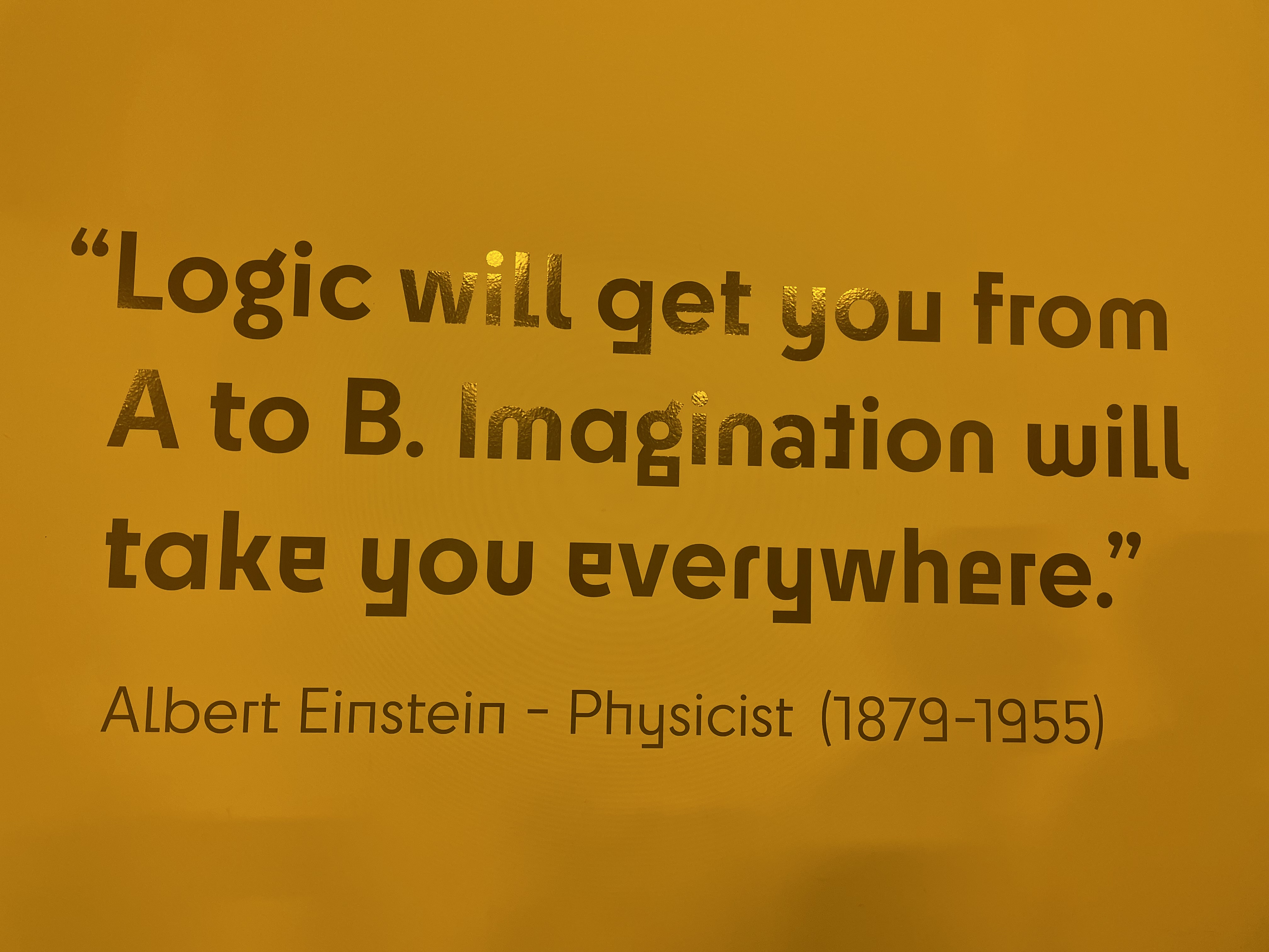 Six people standing in front of a large wooden sculpture of an animal resembling a fox in a green forest.