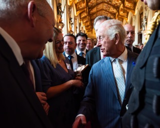 Wood shelter with stacked logs on both sides and a path leading through, with signs reading 'Bugginghum' and 'Palace' under green leafy trees.