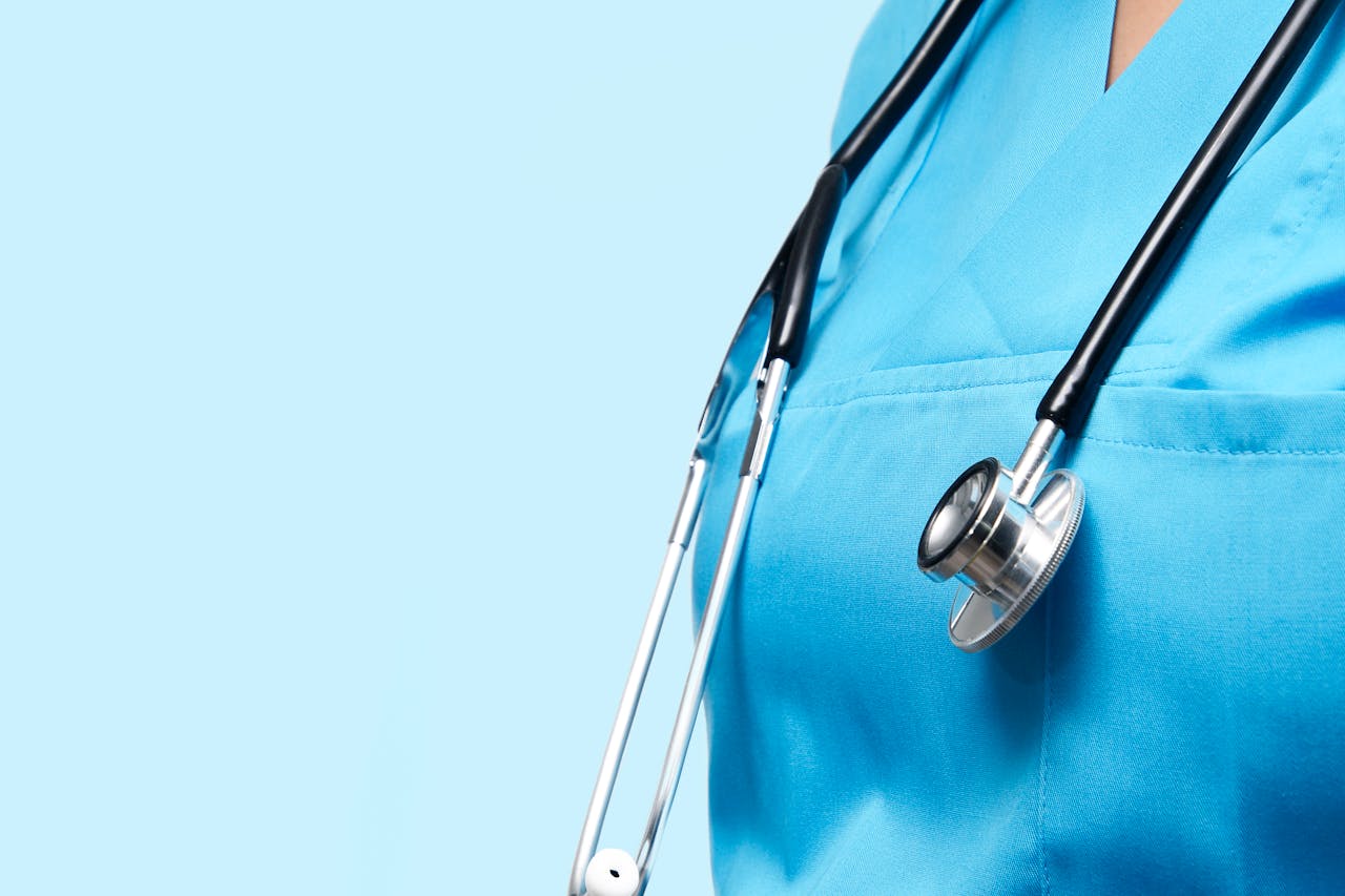 Primo piano di una persona in camice medico azzurro con stetoscopio nero al collo.