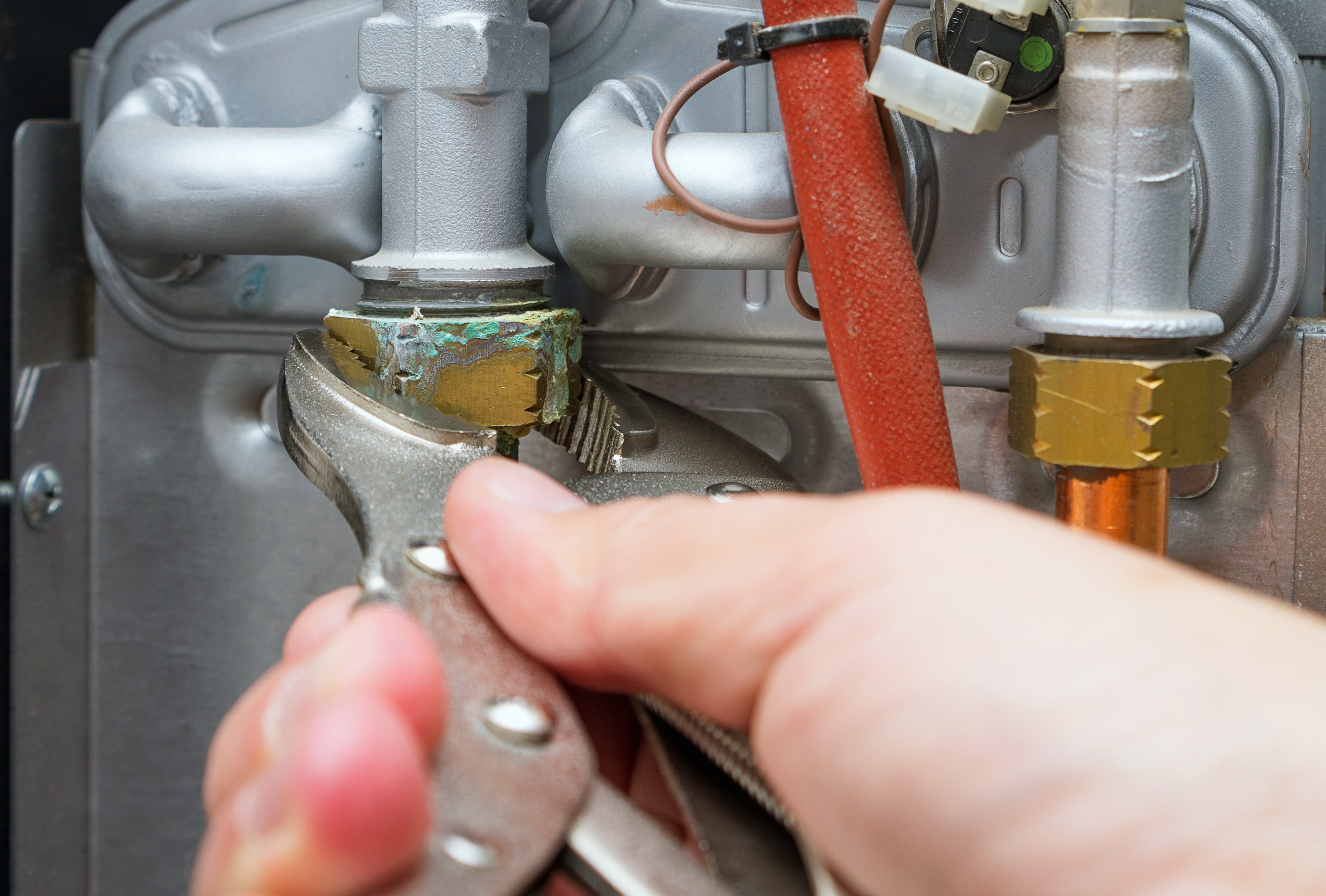 Technician wearing gloves and a blue cap installing or servicing an outdoor air conditioning unit on a white wall.