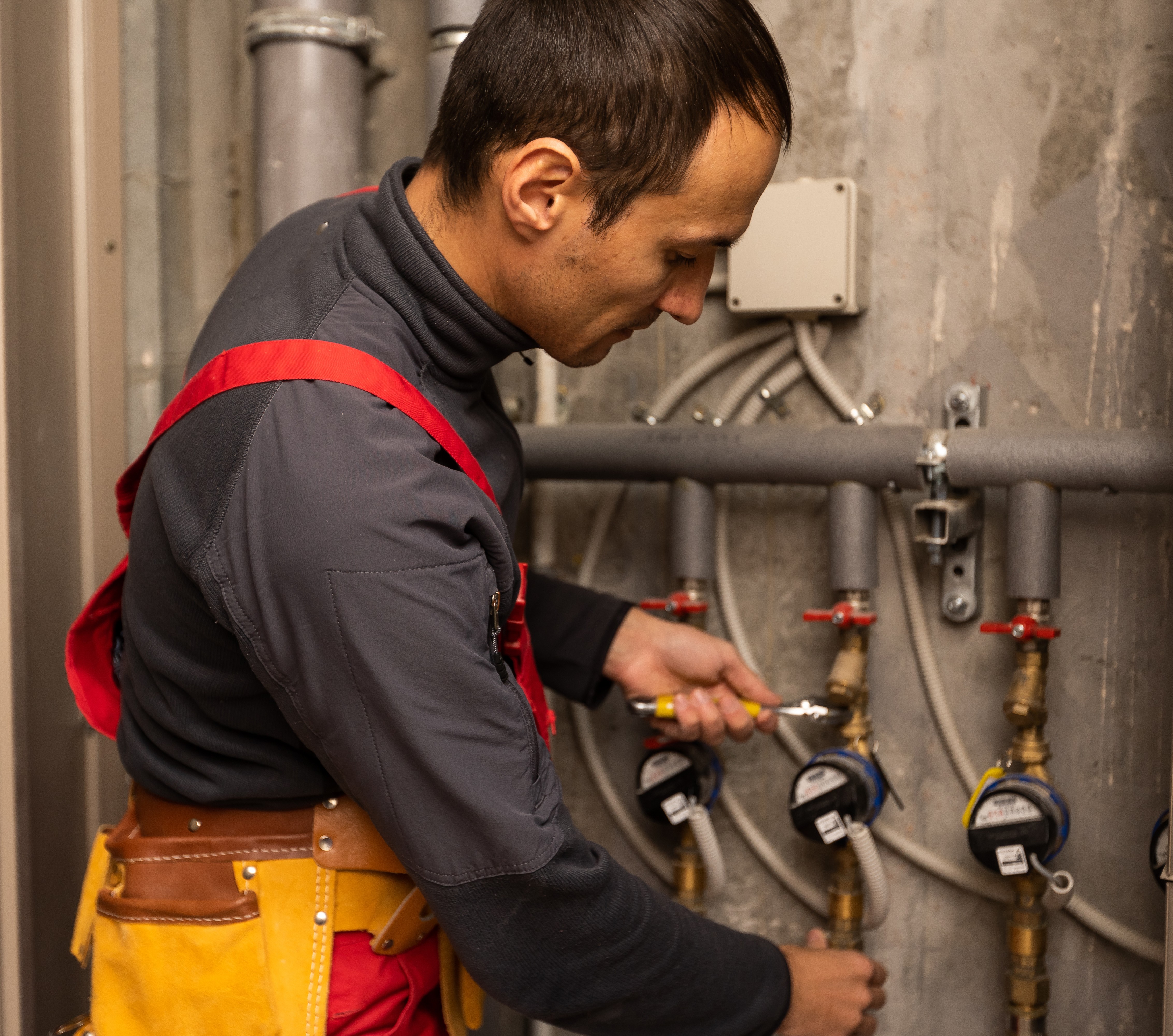 Technician wearing gloves and a blue cap installing or servicing an outdoor air conditioning unit on a white wall.