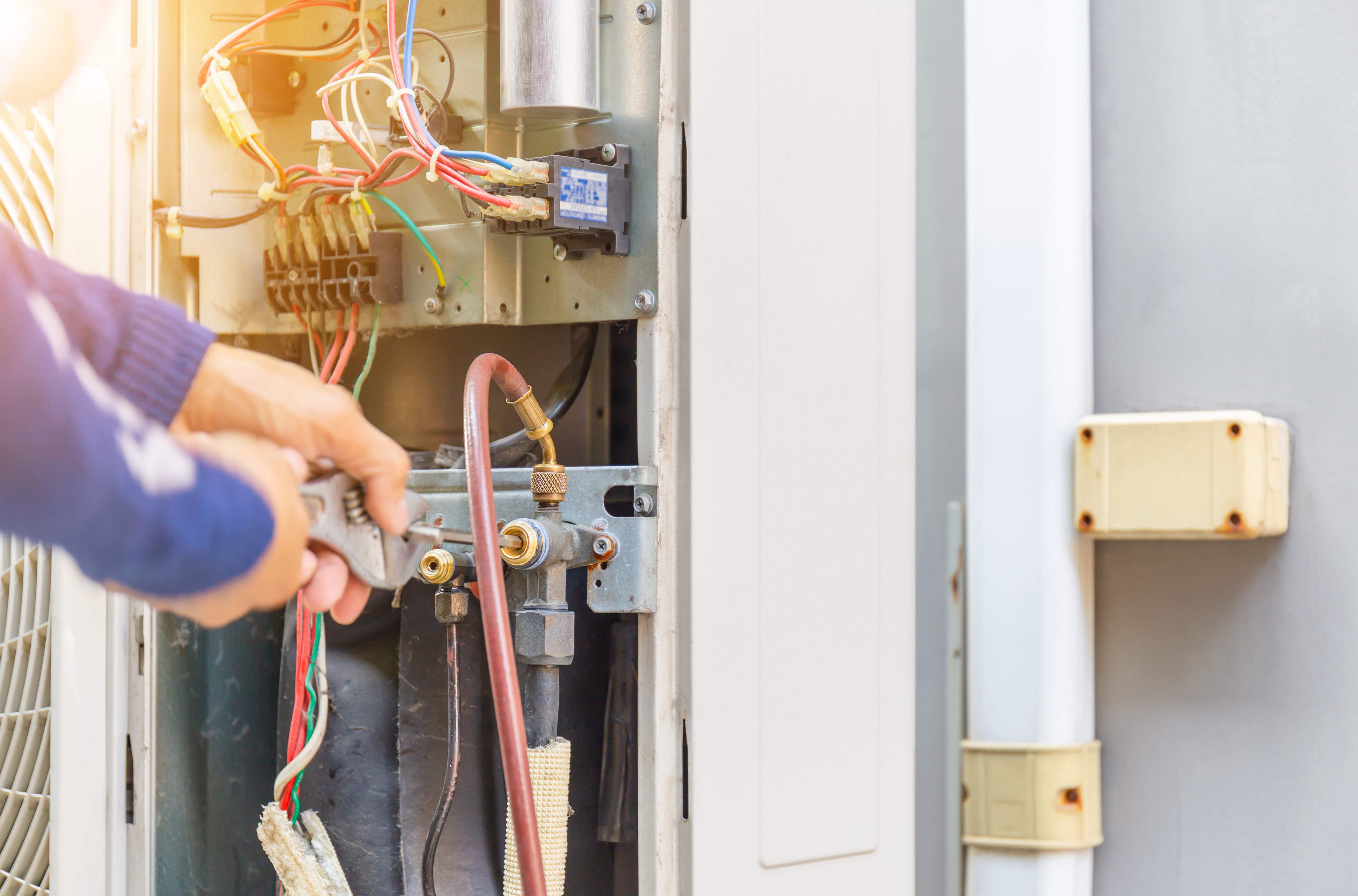 Technician wearing gloves and a blue cap installing or servicing an outdoor air conditioning unit on a white wall.