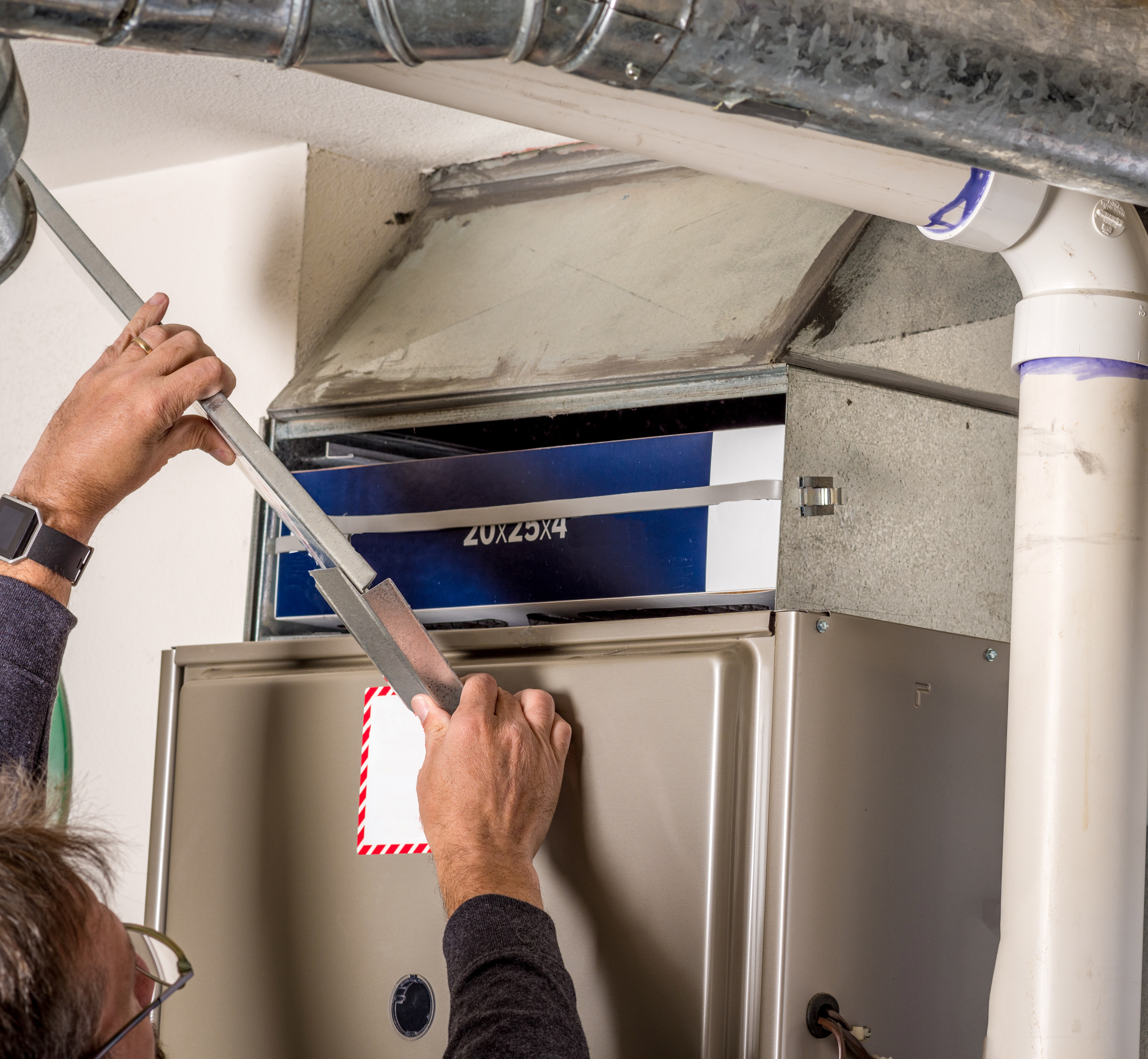 Technician wearing gloves and a blue cap installing or servicing an outdoor air conditioning unit on a white wall.