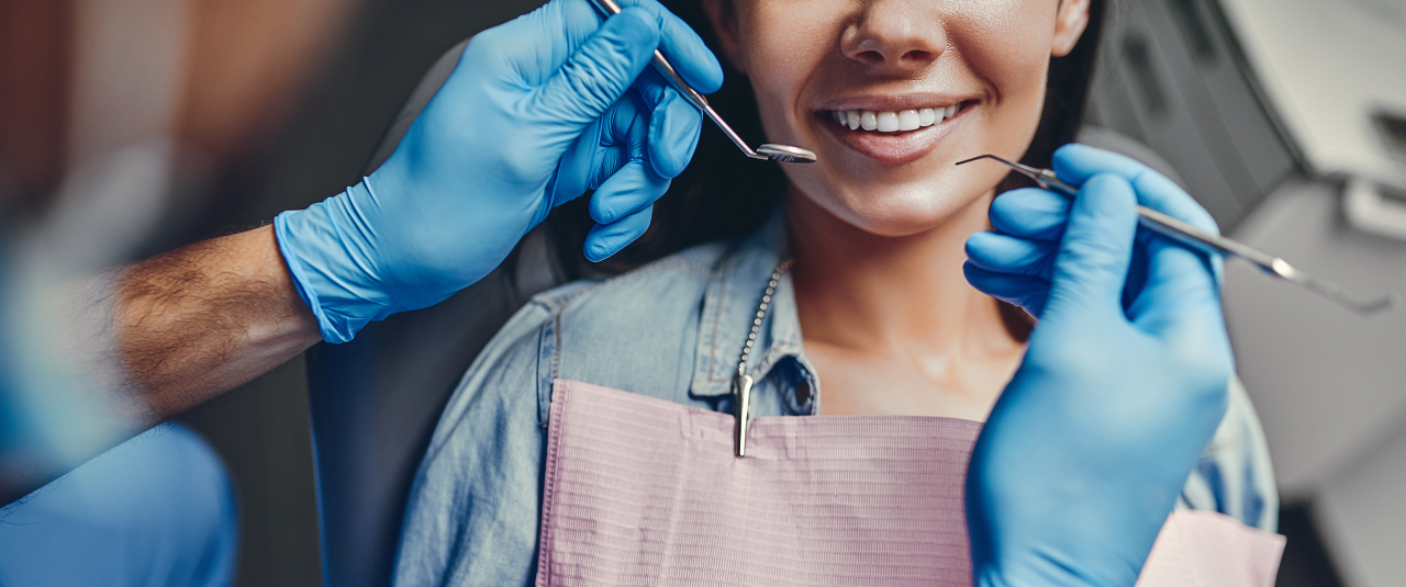Dentist wearing blue gloves holding dental tools near smiling patient in dental chair.