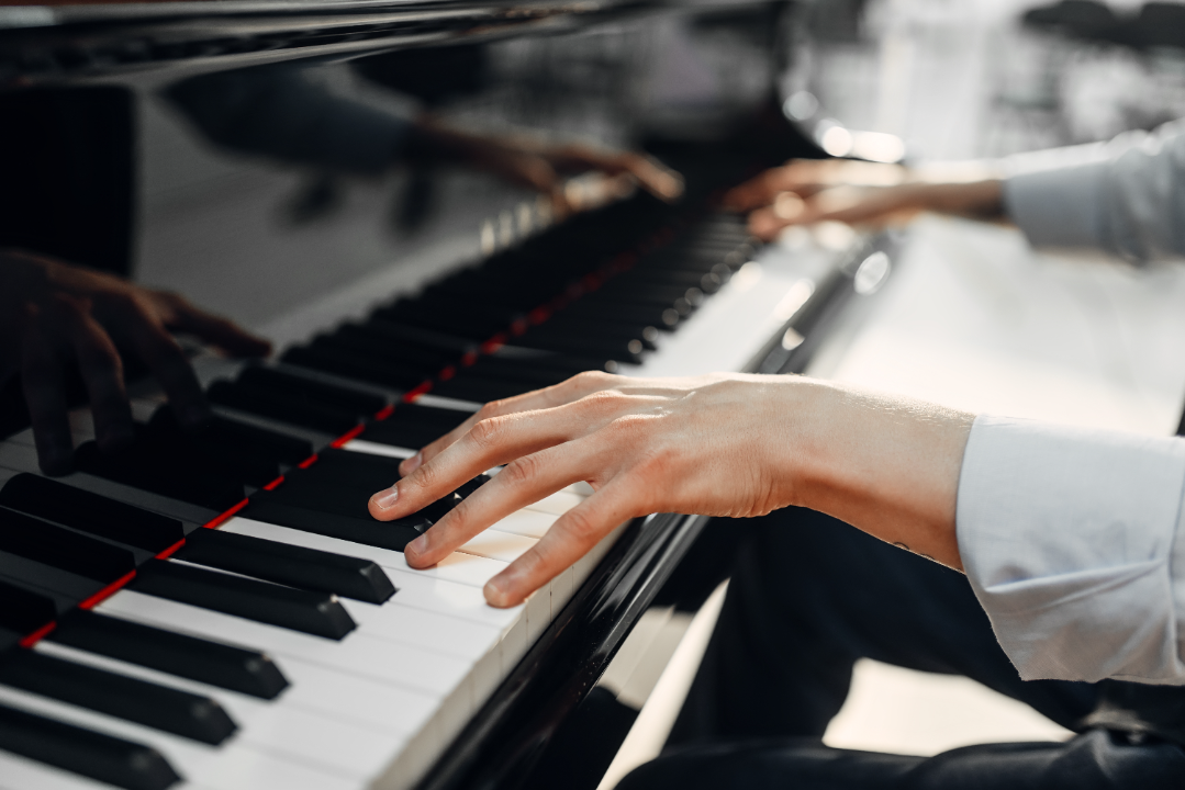 Close-up of hands playing a piano keyboard with reflection on the polished piano surface.