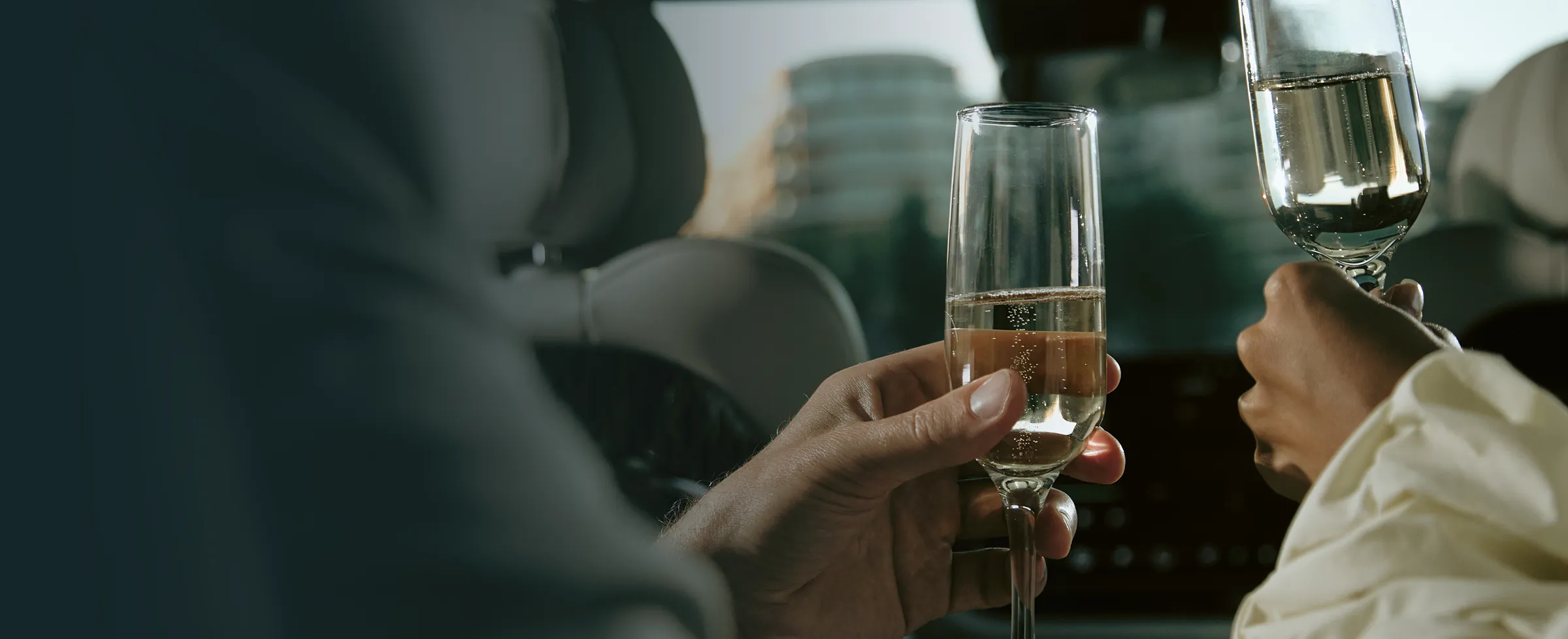 Two people holding champagne glasses inside a car, with buildings visible through the window.