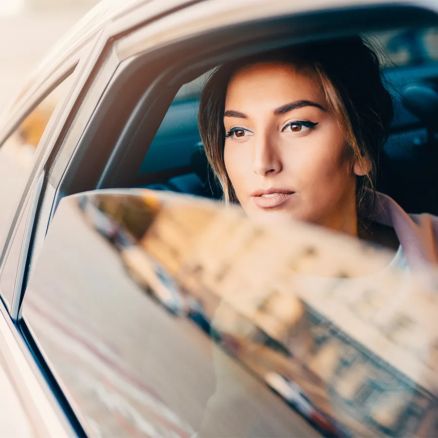 Woman looking thoughtfully out of a car window with blurred cityscape reflection.