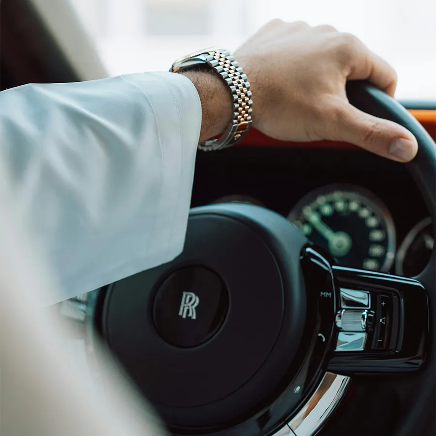 Close-up of driver’s hand wearing a silver watch on the steering wheel of a Rolls-Royce car.