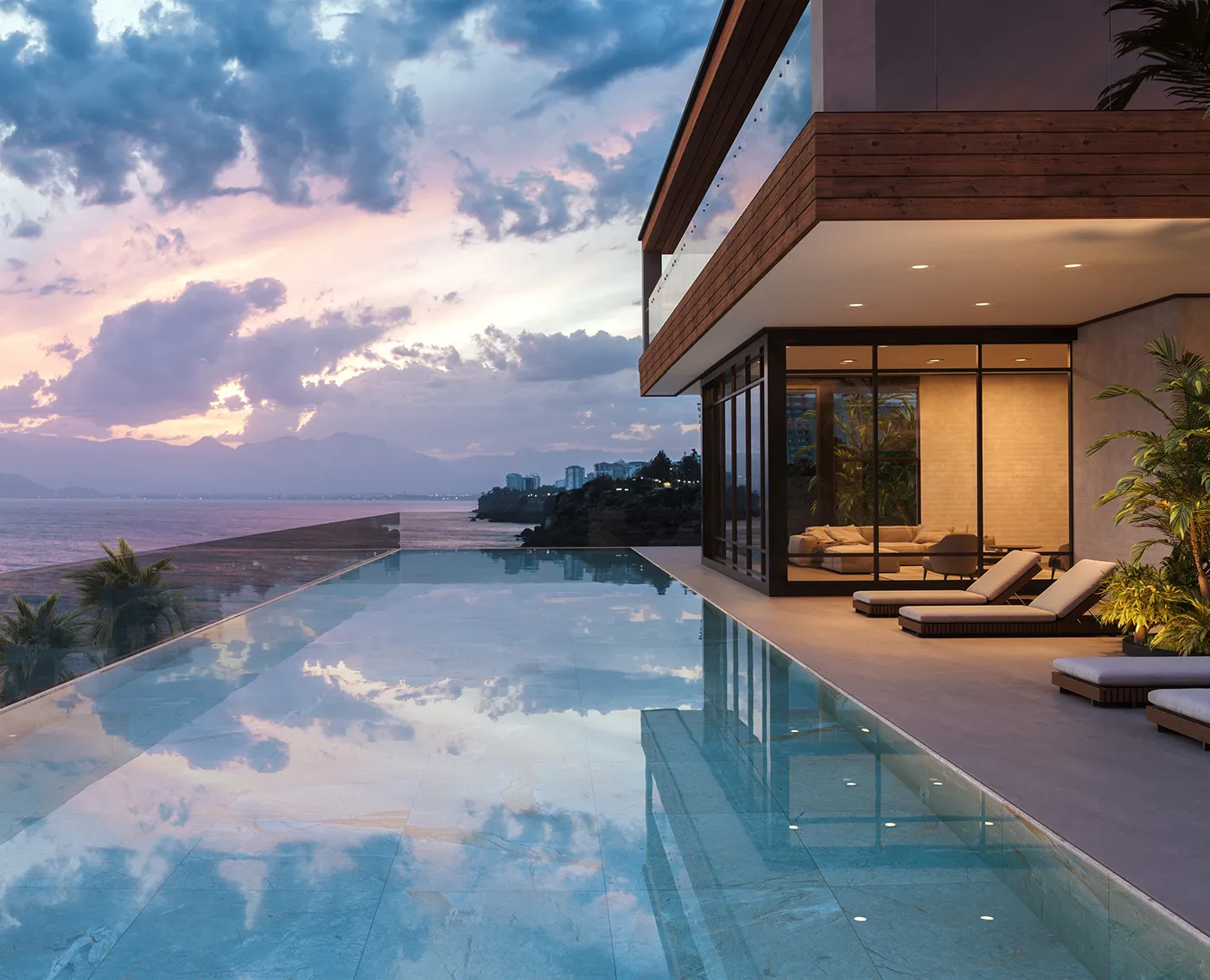 Modern house with large windows next to an infinity pool reflecting a cloudy sunset sky overlooking the sea.