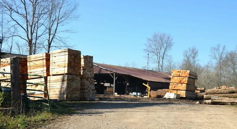 Timber stacked in a builders merchant yard alongside a storage building