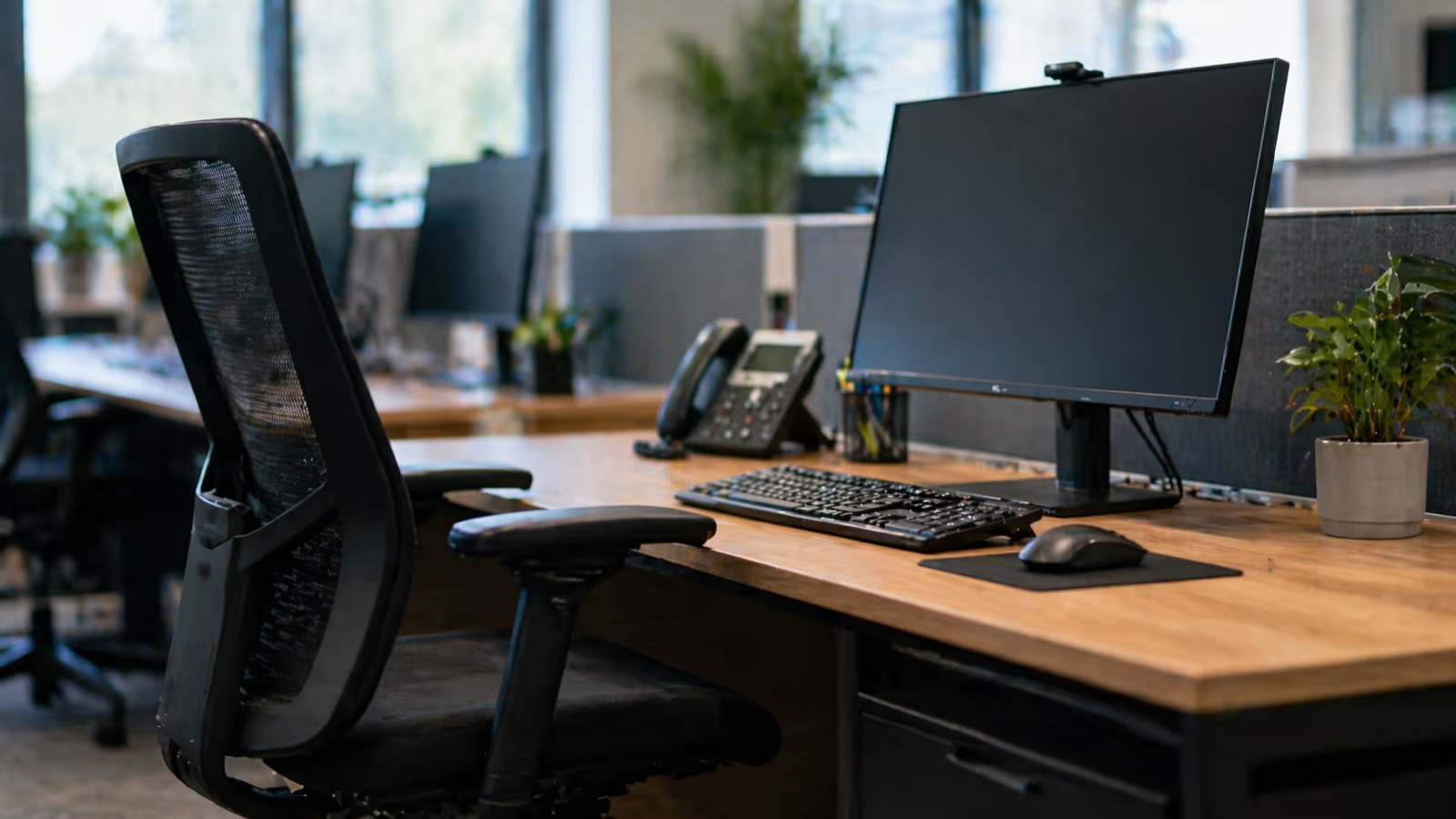 An office workstation with an adjustable mesh chair, a monitor, keyboard and mouse on a wooden desk