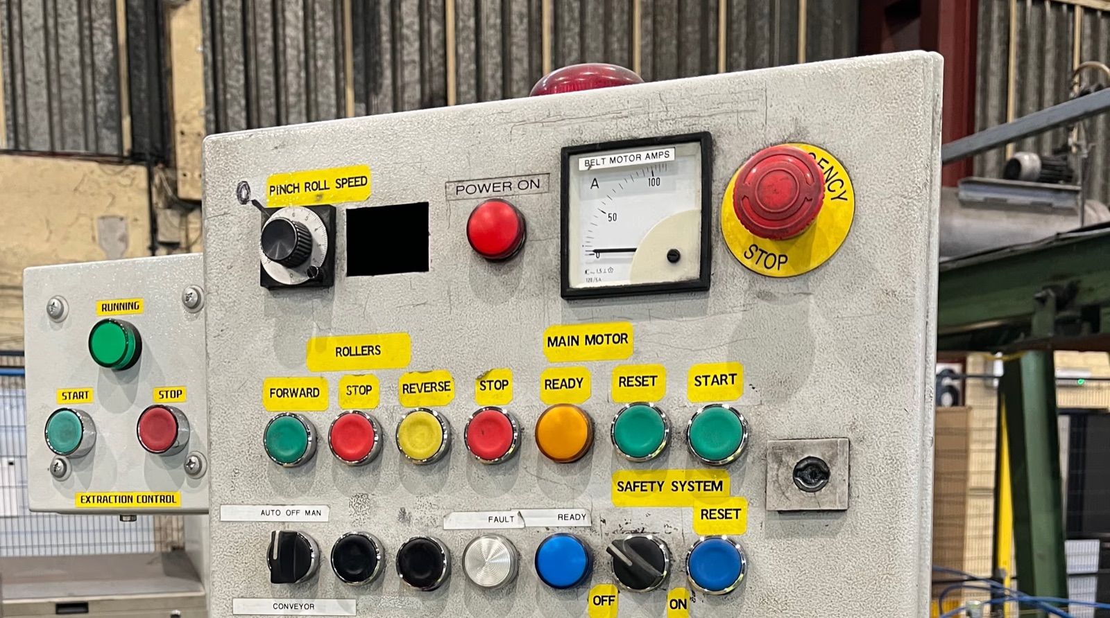 Machine control panel with an emergency stop button, an ammeter and coloured start and stop buttons in a factory