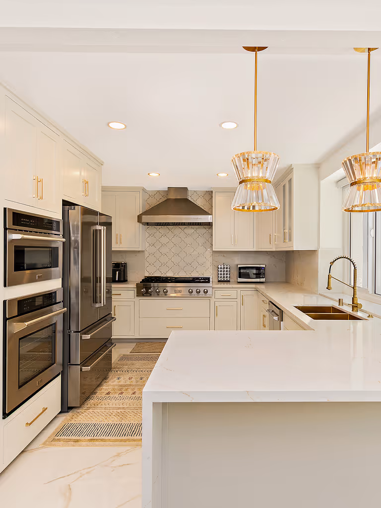 Modern kitchen with white cabinetry, stainless steel appliances, marble countertops, gold fixtures, and two pendant lights above the island.