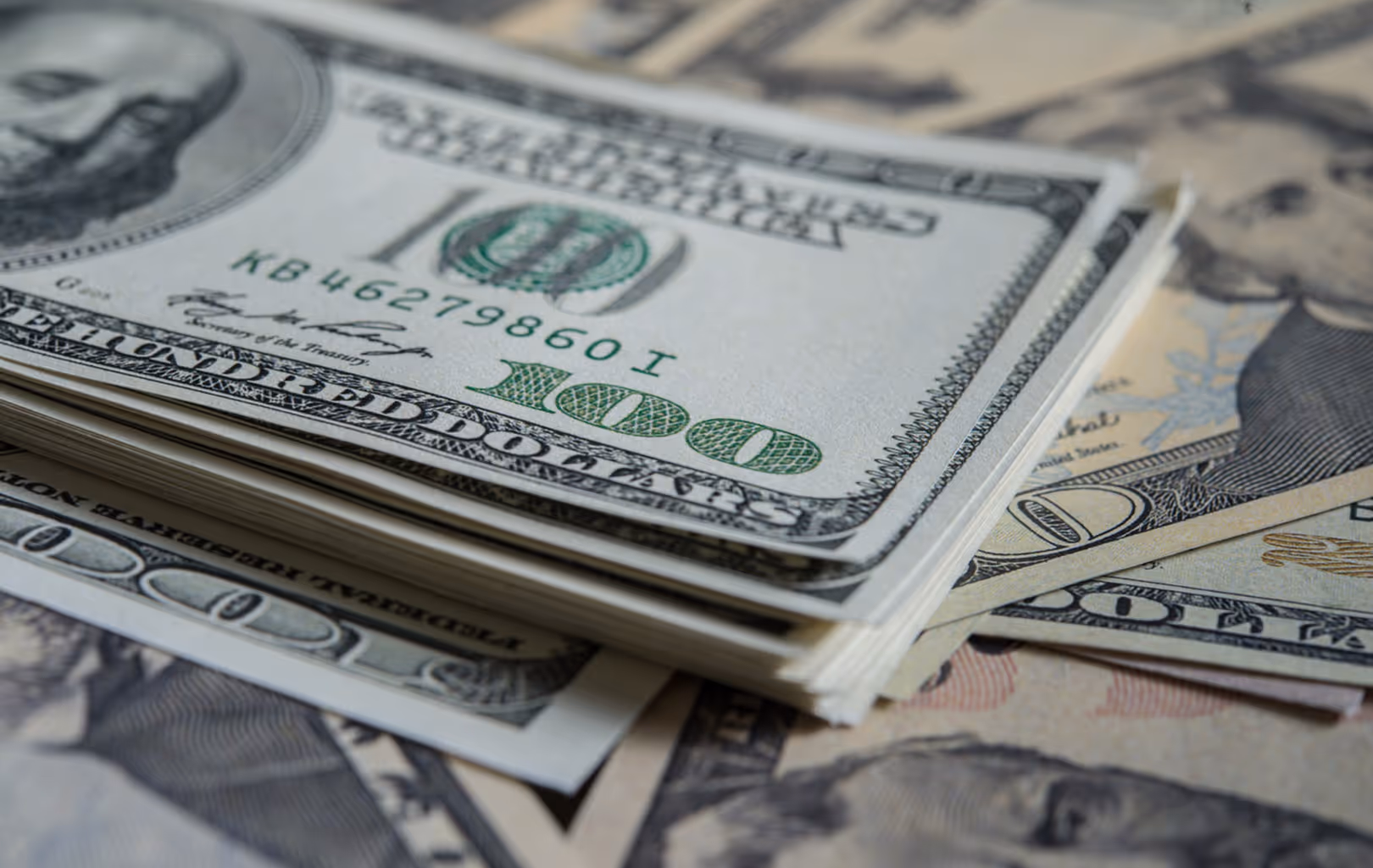 Stack of one hundred dollar bills with the top bill showing the number 100 and portrait of Benjamin Franklin.