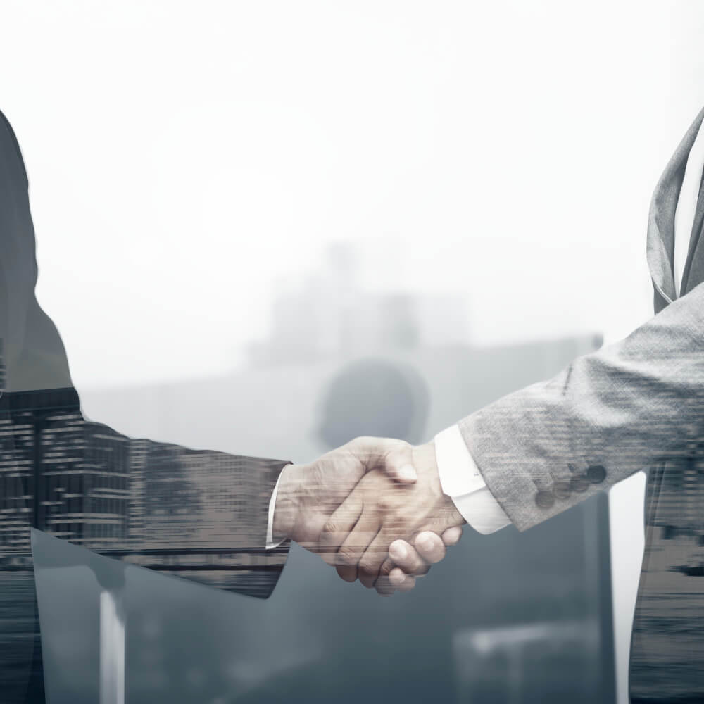 Two businesspeople in suits shaking hands with a cityscape overlay, symbolizing partnership or agreement.