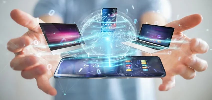 Person holding holographic projections of a smartphone, laptop computers, and a globe, symbolizing digital connectivity and technology.