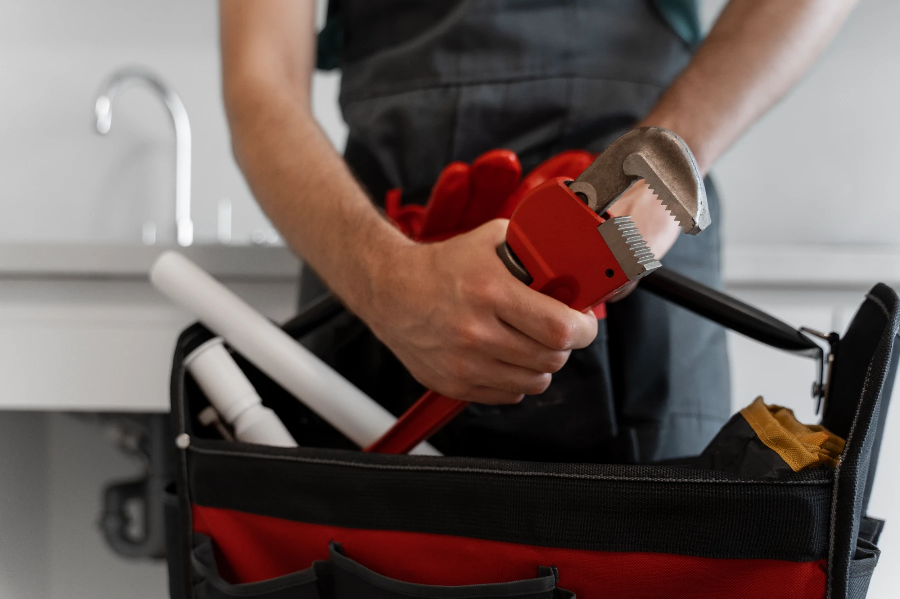Idraulico che tiene una chiave inglese rossa sopra una borsa con attrezzi da lavoro in cucina.