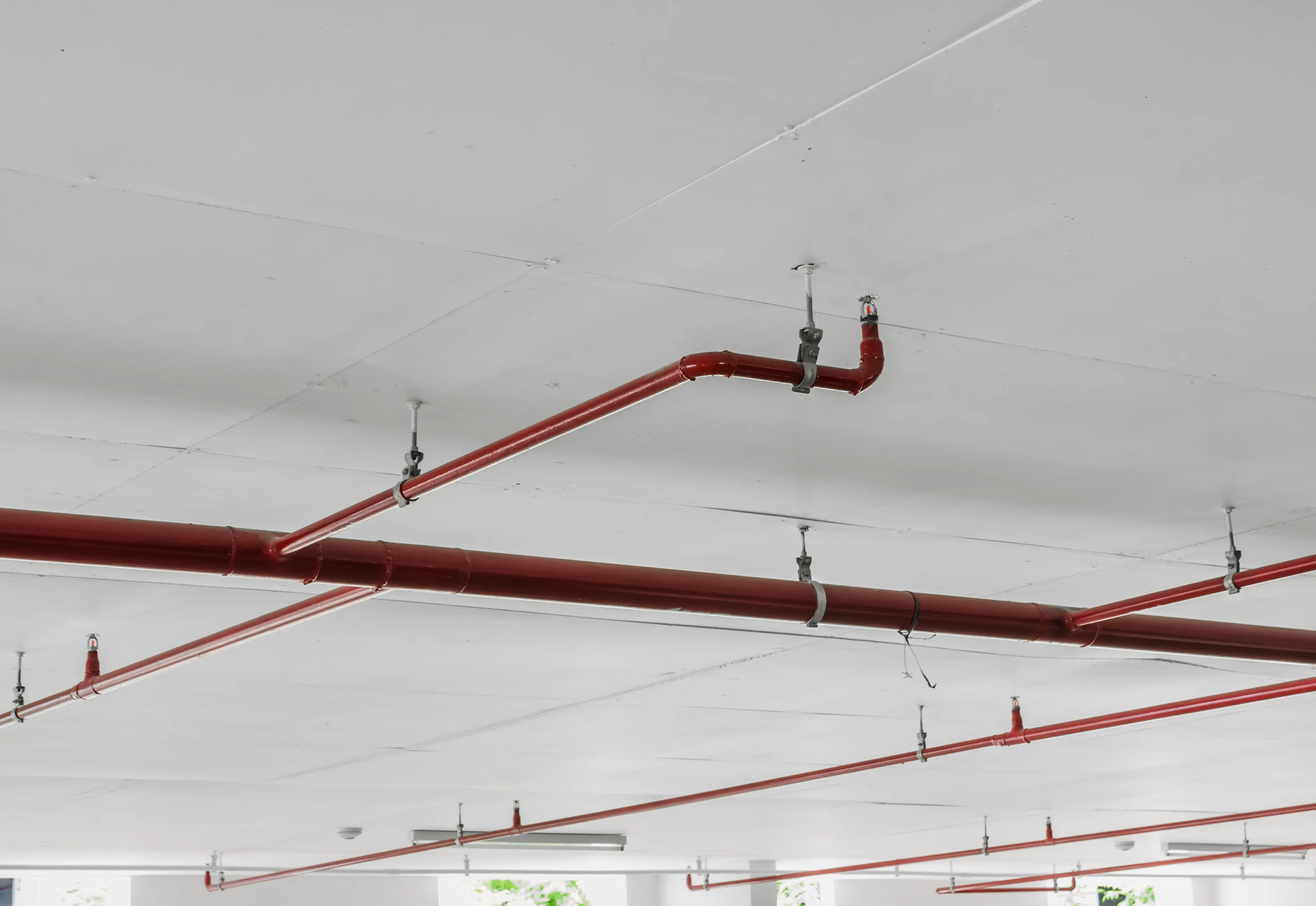 Tubi rossi dell'impianto antincendio montati su soffitto bianco in un parcheggio coperto.