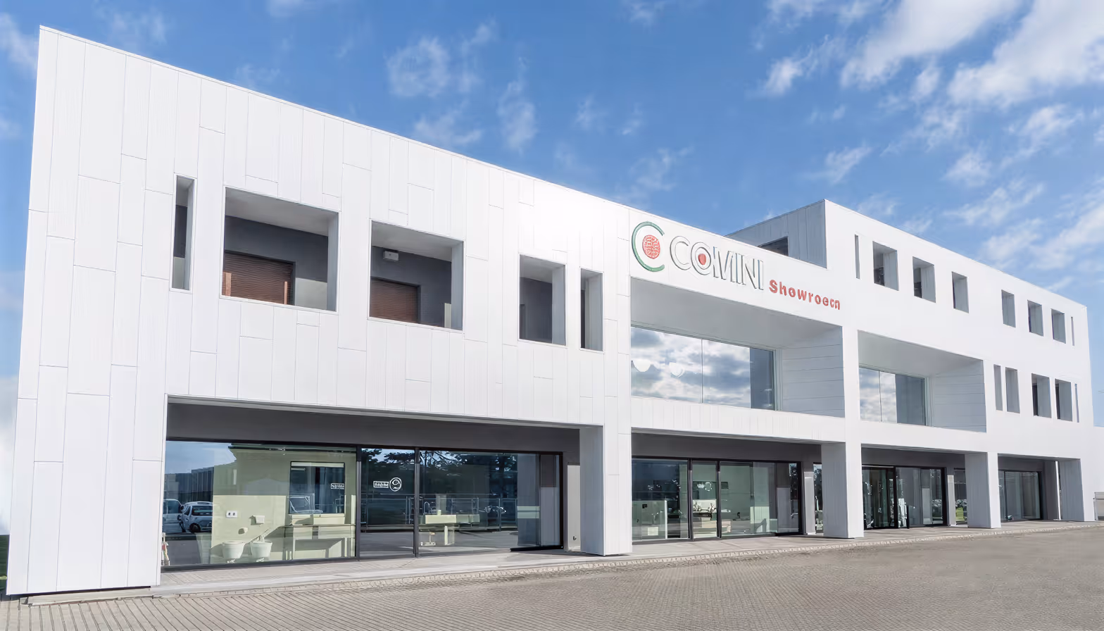 Edificio bianco moderno con grandi vetrate e insegna "COMINI showroom" sotto un cielo blu.