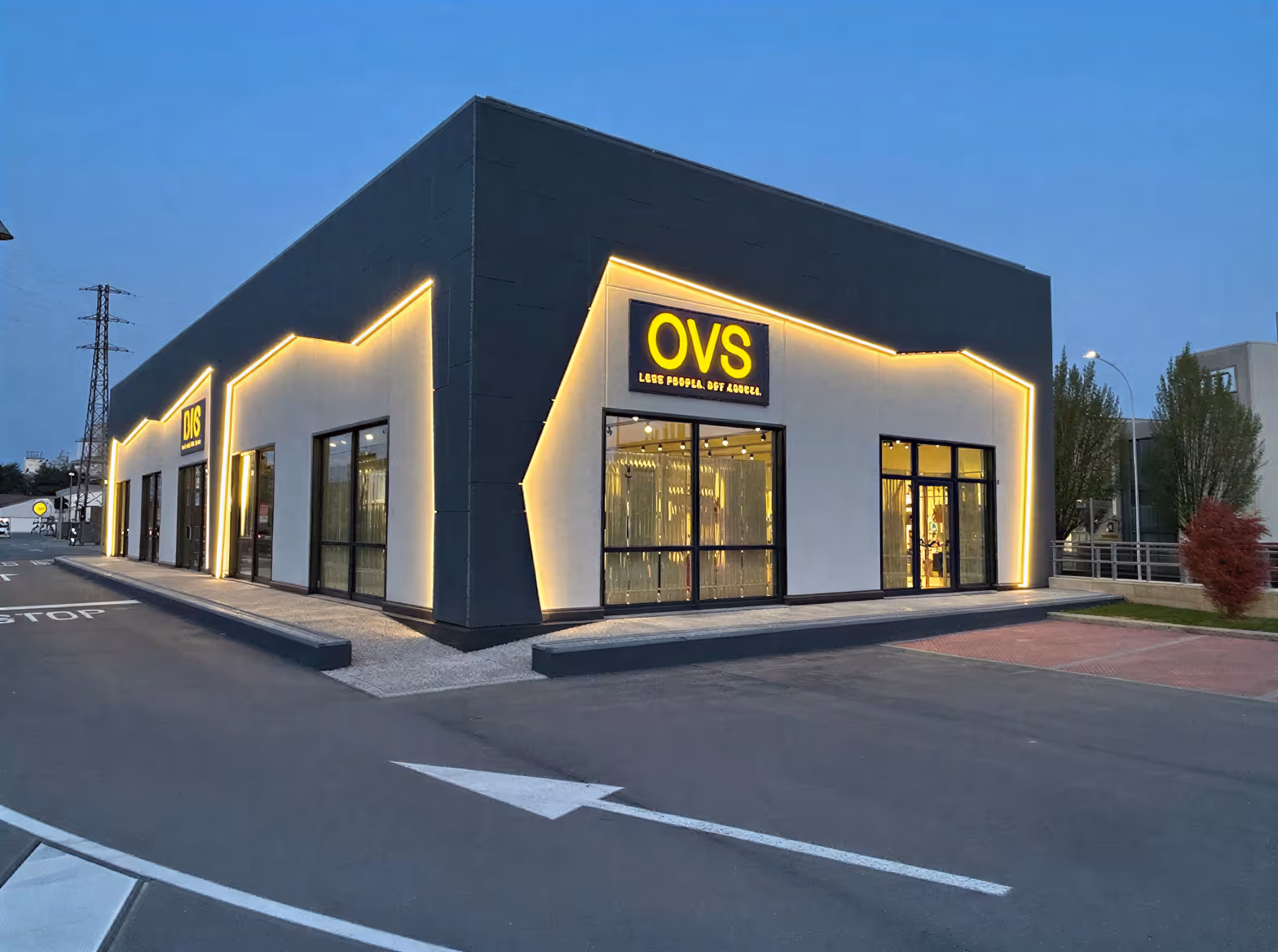 Edificio moderno con luci gialle a LED e vetrine di negozi OVS e DIS al crepuscolo.