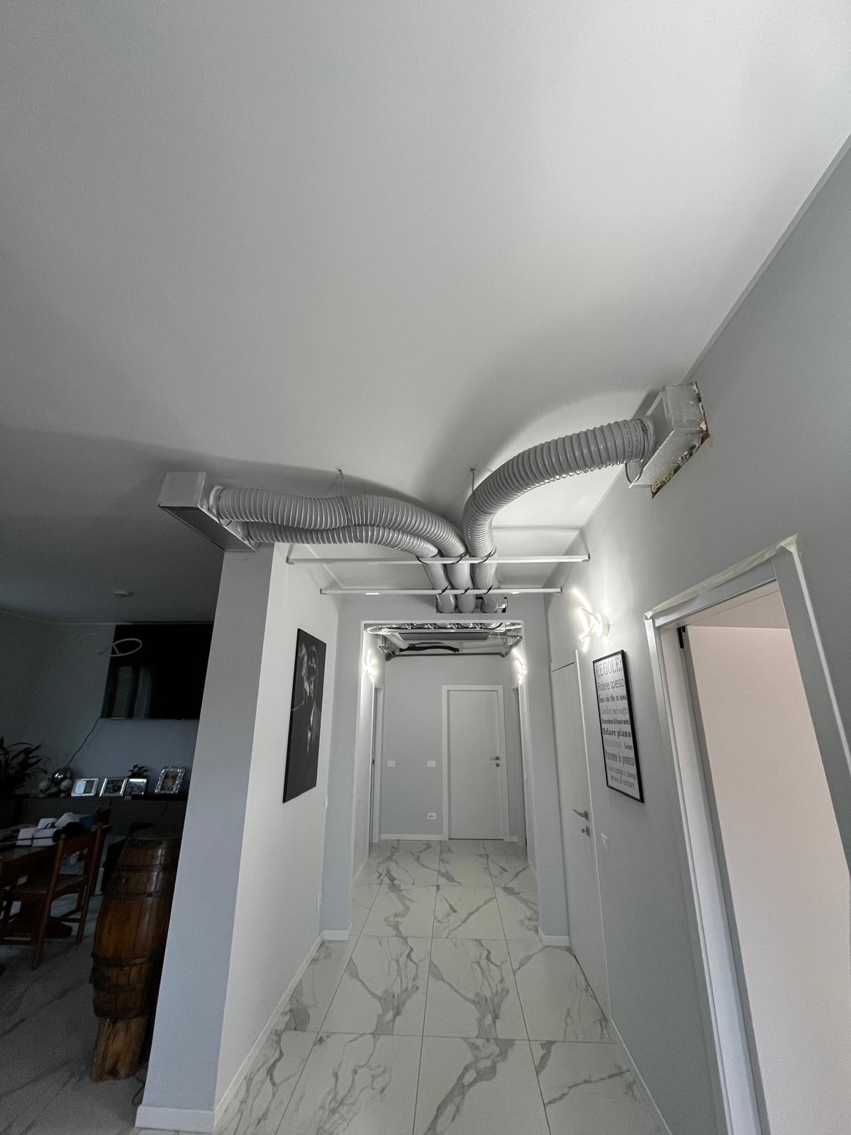 Corridoio moderno con pavimento in marmo, tubi grigi flessibili sul soffitto e pareti bianche e grigie.