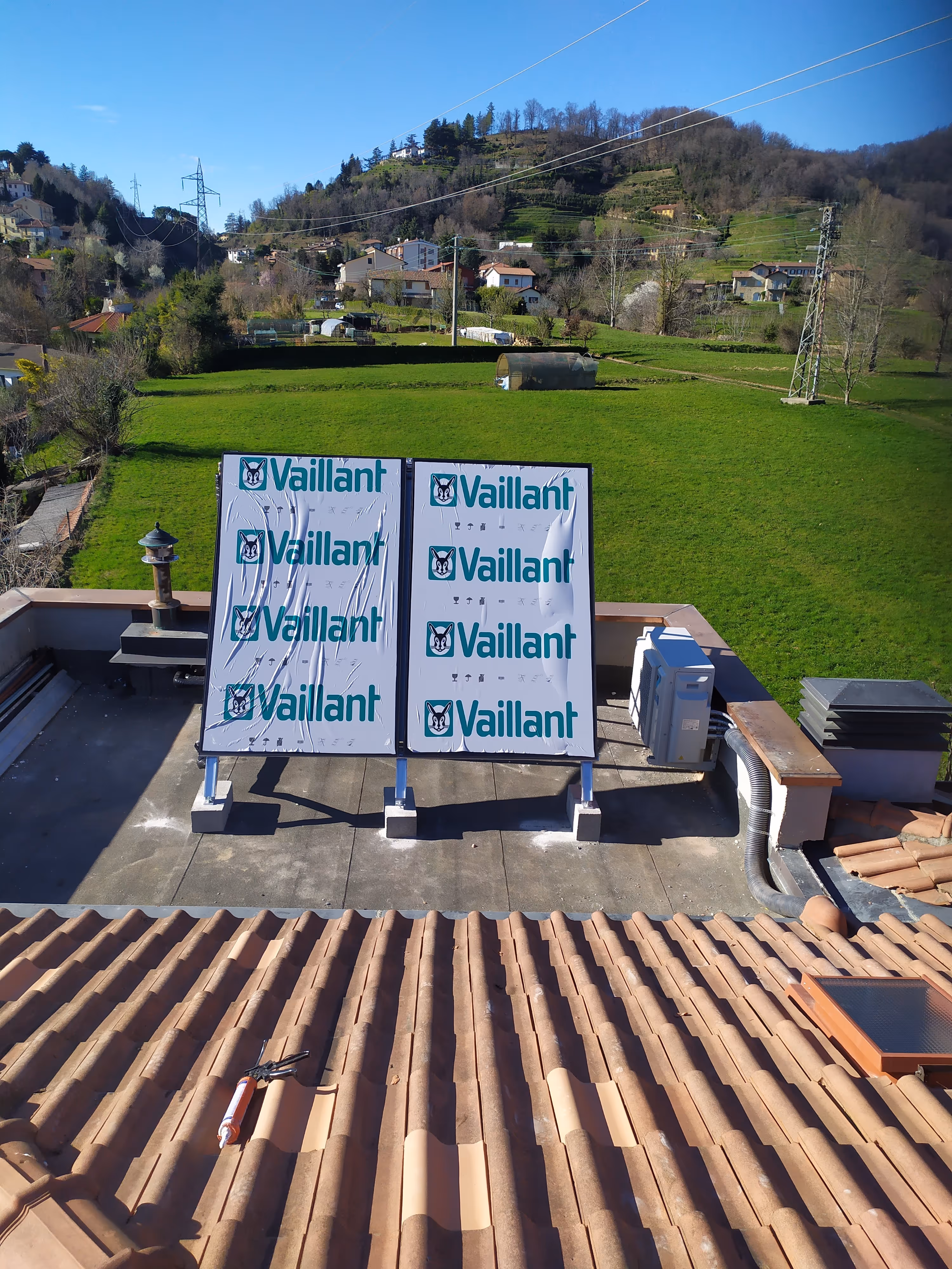 Due pannelli coperti da protezioni con logo Vaillant su un tetto con campi verdi e colline sullo sfondo.